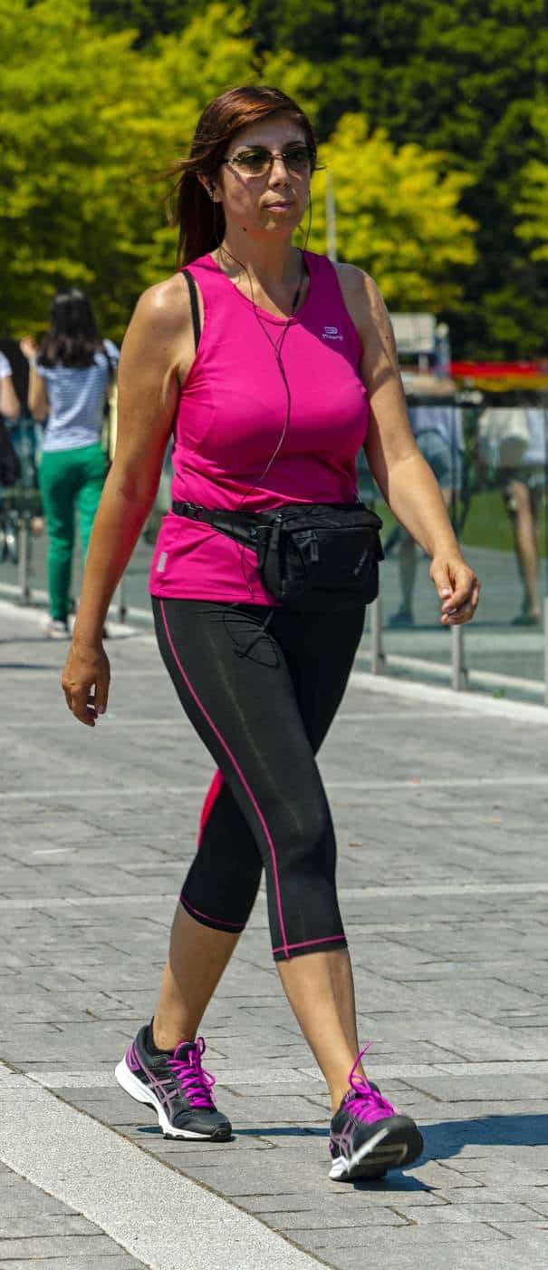 A woman in a pink top walking briskly along a waterfront promenade